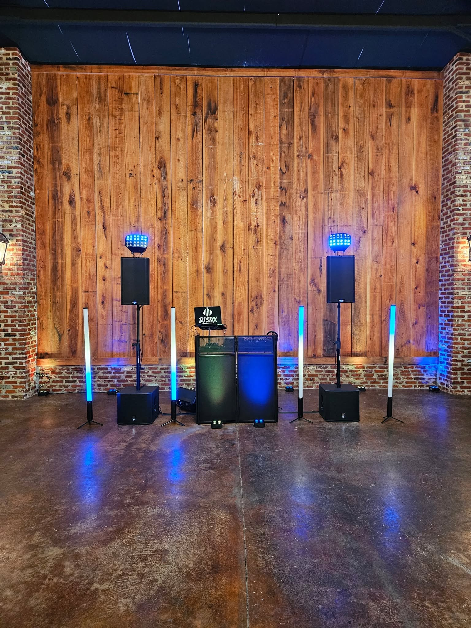 ESM DJ booth with speakers and blue LED tube lighting against a rustic wood backdrop
